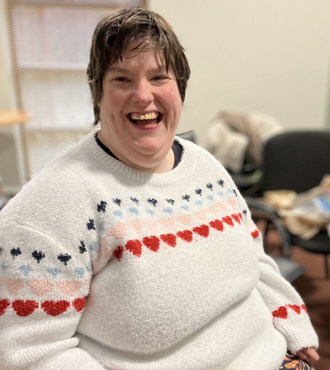 Chelsea who has joined the NHS Learning Disability and Autism Advisory group sat in a chair smiling at the camera.