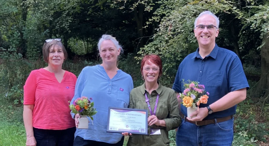 Three women and one man holding flowers and a certificate.